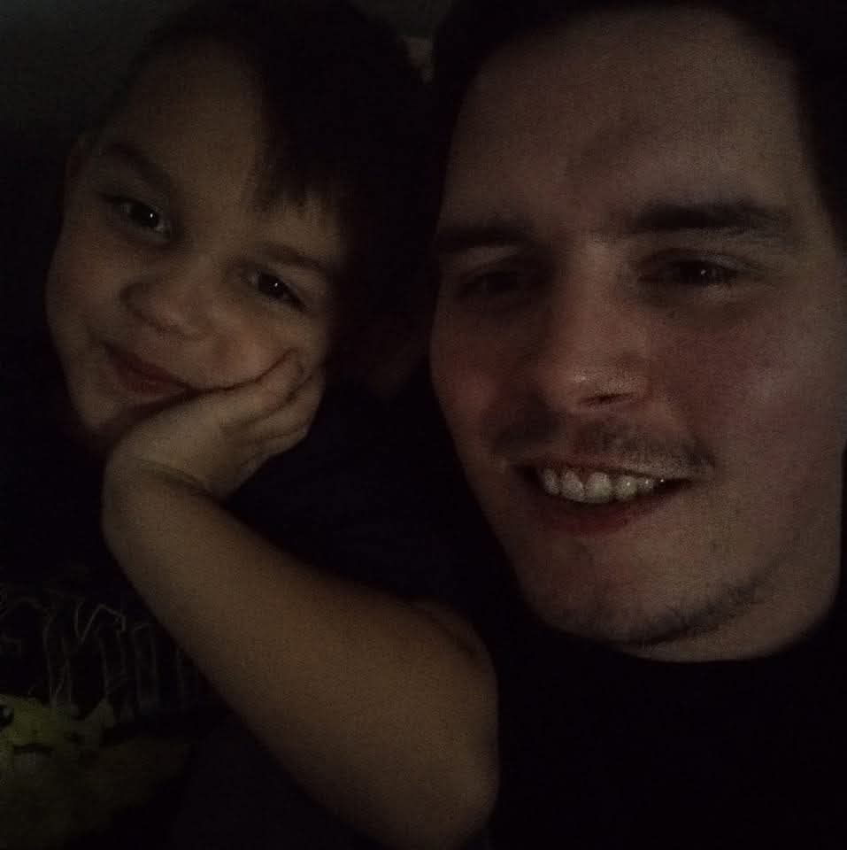 A man and child smiling closely together in a dimly lit setting.