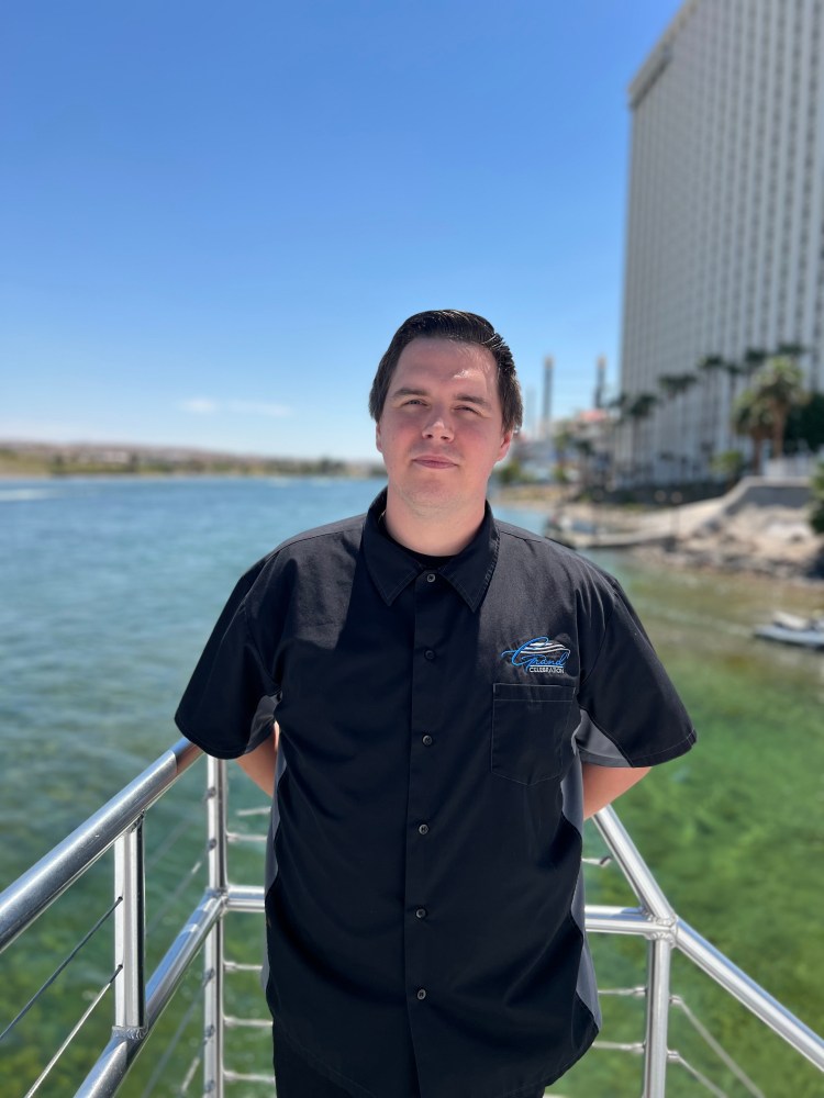 Person in black shirt stands on railing by water, tall building in background.