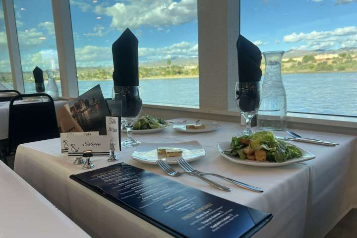 Table set for two with salads, facing large windows overlooking a river on a sunny day.