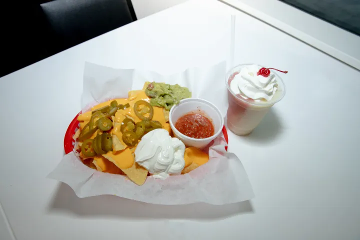 Nachos with cheese, jalapeños, sour cream, guacamole, salsa; milkshake topped with whipped cream and cherry.