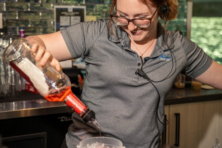 Woman pouring liquid into a measuring cup in a kitchen or bar setting.