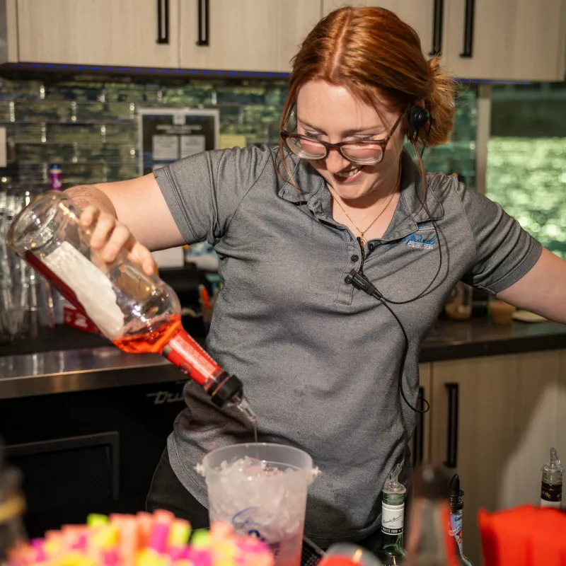 Woman pouring liquid into a measuring cup in a kitchen or bar setting.