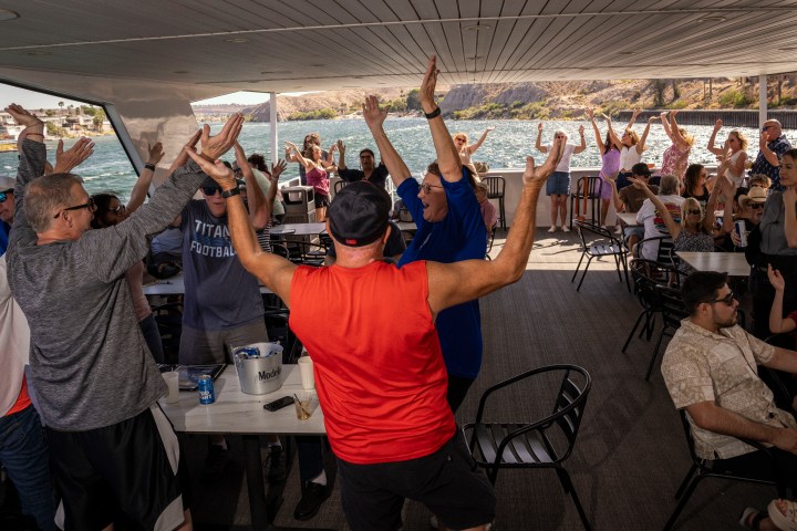 Group of people cheering under a shaded deck near water.