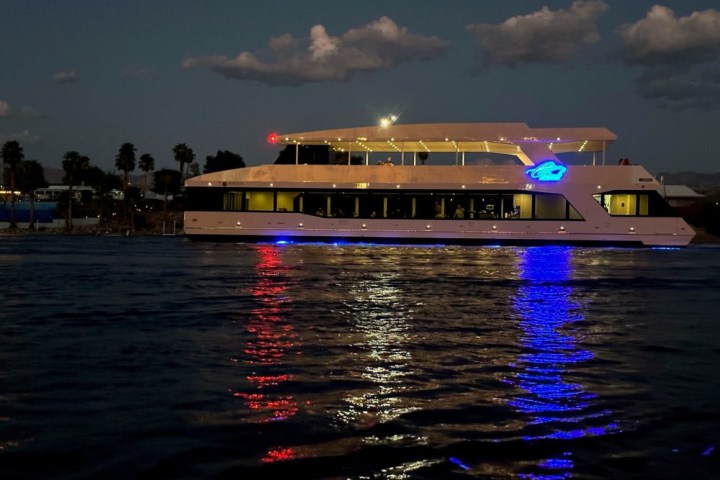 Illuminated yacht on water at night with blue and red lights reflecting.