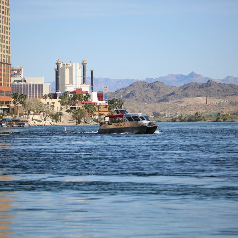 Boat named London Jet on river with casino buildings and mountains in the background.
