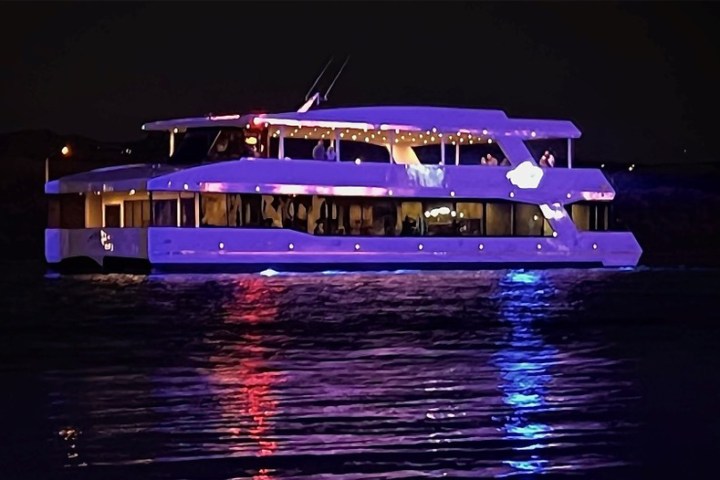 A lit-up yacht on water at night, reflecting colorful lights.