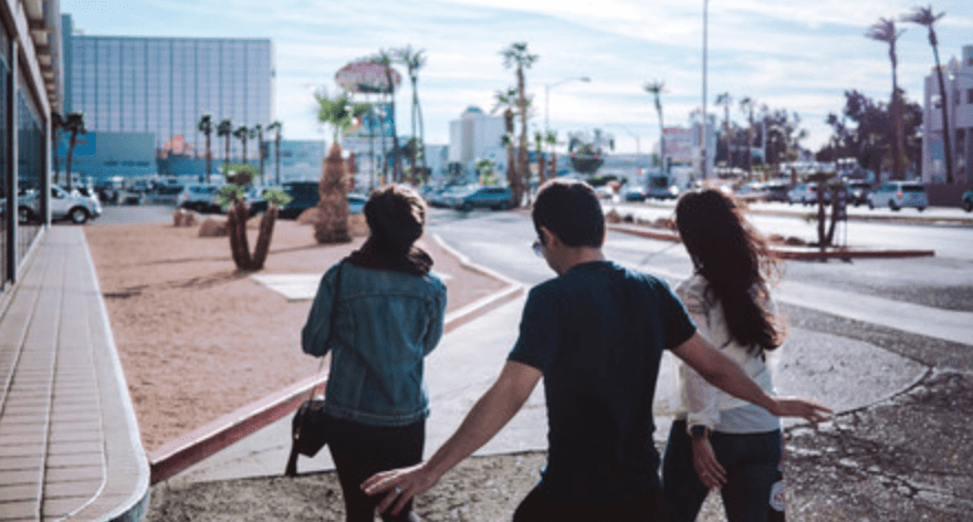 Three people walking on a street with palm trees and buildings in the background.
