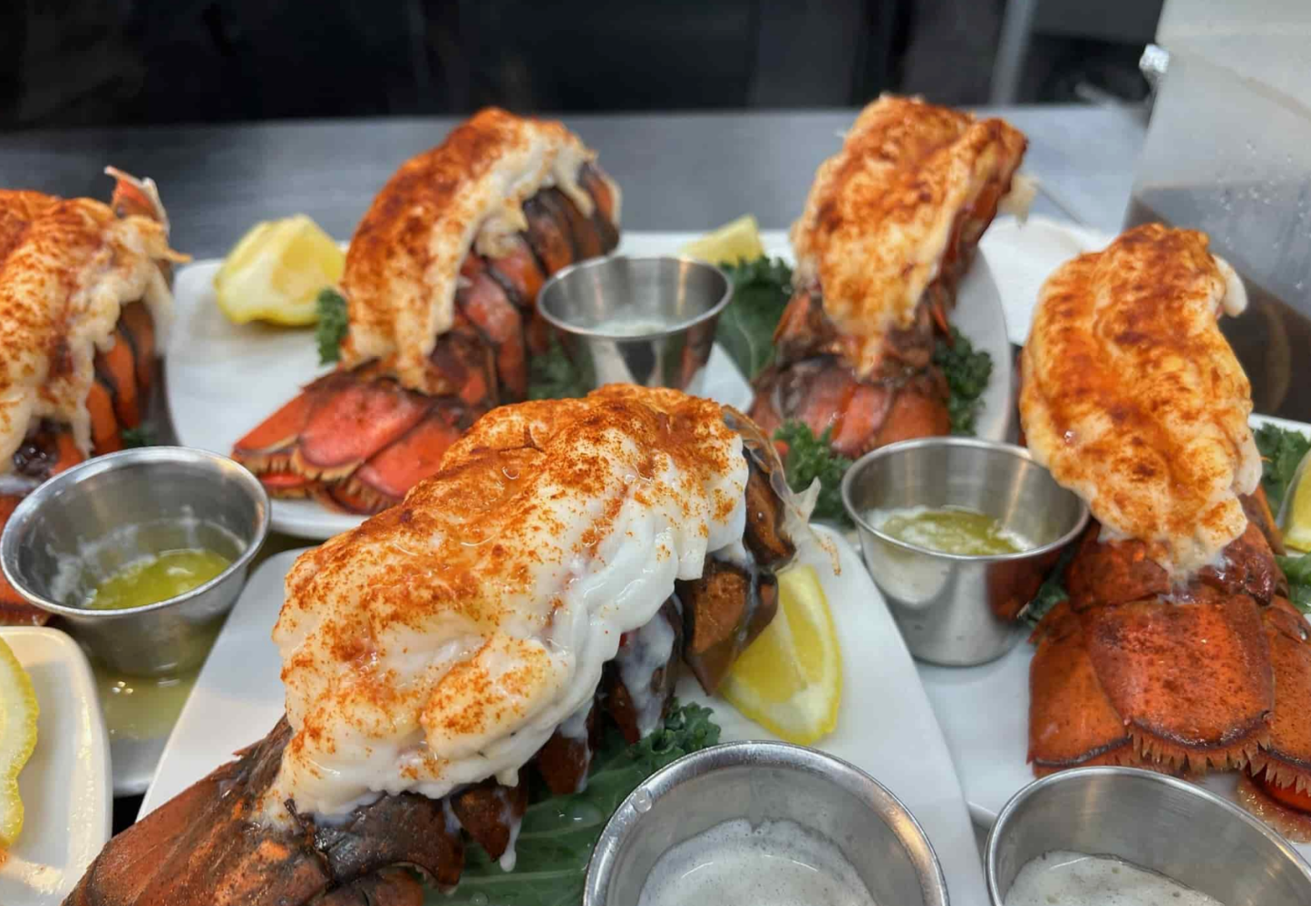 Several baked lobster tails with butter and lemon slices on plates.