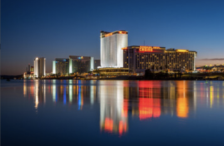 City skyline at dusk with colorful building lights reflected on calm water.