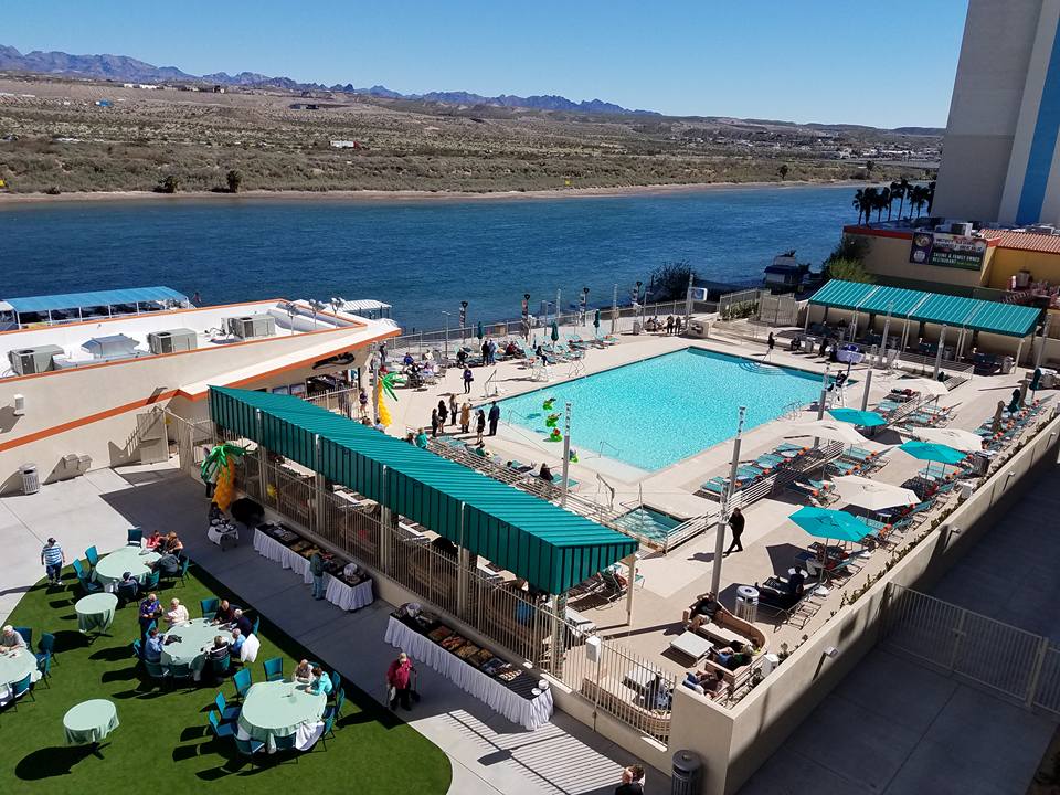 Hotel pool area with loungers and umbrellas beside a river, with a desert landscape in the background.