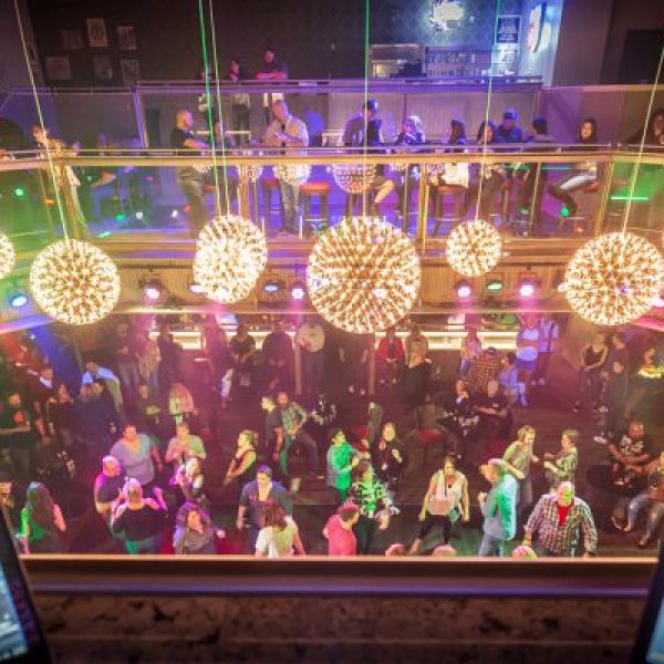 View from DJ booth of a lively nightclub with dancing crowd and large spherical lights.