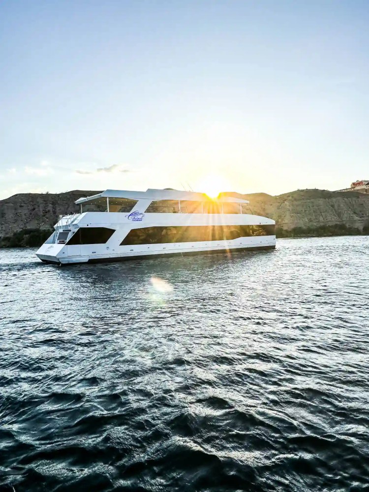 White yacht on calm water with sun setting behind distant hills.