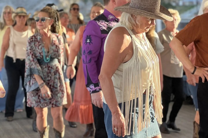People line dancing in casual western attire under a canopy.