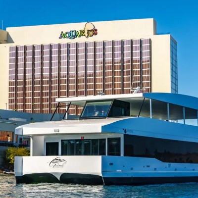 Modern white yacht on water with a large hotel building named Aquarius in the background.