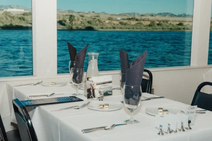 Elegantly set dining table by window with water view and folded napkins.