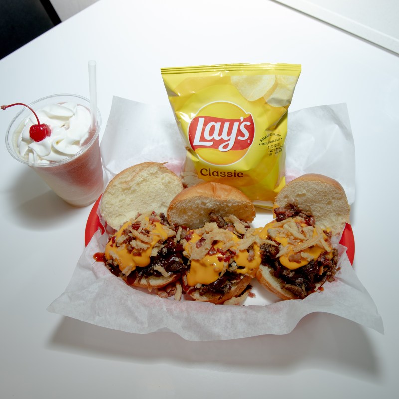 Sliders with cheese, Lay's chips, and a cherry-topped milkshake on a table.