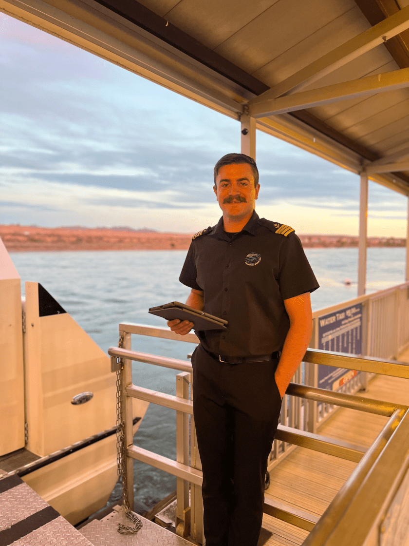 Man in uniform holding a tablet on a dock at sunset.