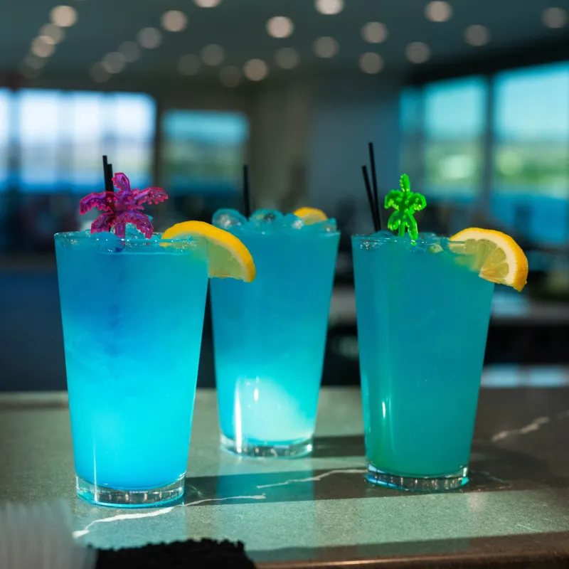 Three blue cocktails with lemon slices on a bar counter.